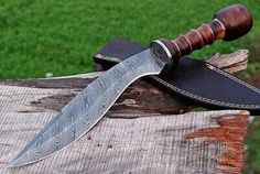 a knife is sitting on top of a piece of wood with a leather sheath around it