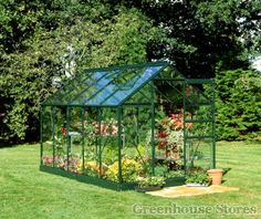 a small green house sitting on top of a lush green field with lots of flowers