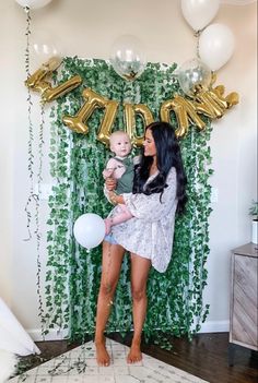 a woman holding a baby while standing in front of balloons