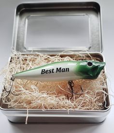 a green and white fishing lure in a metal box with the words best man on it