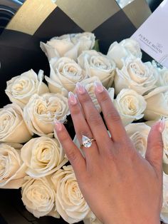 a woman's hand with a diamond ring on top of white roses