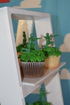 two cupcakes with green frosting on top of a shelf in the shape of soldiers