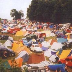 a large group of tents and cars in a field with trees on the other side