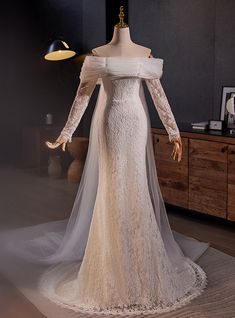 a white wedding dress on display in a room with dark walls and wooden flooring