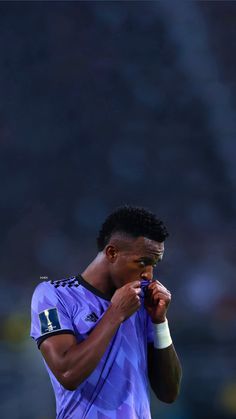 a soccer player is holding his hand to his mouth while looking down at the ground