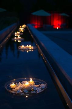 candles are floating on the water in a bowl with white flowers and petals around it