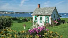 a small white house sitting on top of a lush green field next to the ocean