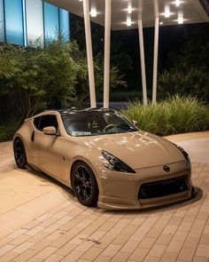 a tan sports car parked in front of a building at night with its lights on