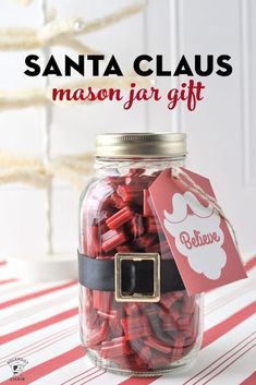 santa claus mason jar gift with red and black candy in it on a striped tablecloth