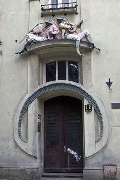 two statues on the side of a building with an open door and window above them