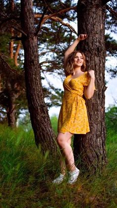 a woman in a yellow dress leaning against a tree