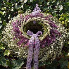 a wreath with purple and white flowers hanging from it's center surrounded by greenery