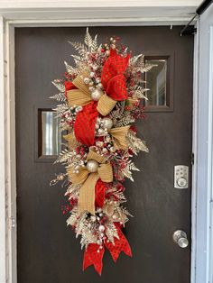 a christmas wreath hanging on the front door with red and gold bows, balls and ornaments