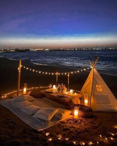 a teepee tent set up on the beach at night with candles lit around it