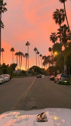 cars parked on the side of a road with palm trees in the background at sunset