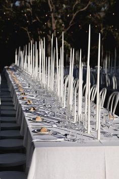 a long table is set up with white candles and place settings for an outdoor event