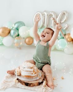 a baby sitting on top of a cake with balloons in the background and a number balloon behind it