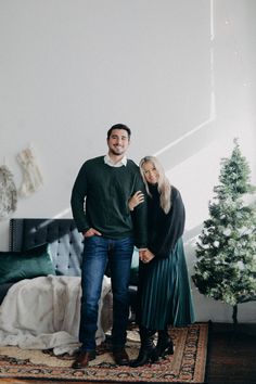 a man and woman standing next to each other in front of a christmas tree on a rug