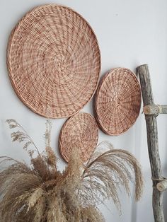 three wicker baskets hanging on the wall next to a wooden stick and some dry grass