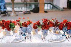 red flowers in blue and white vases on a table set with silverware, napkins and utensils