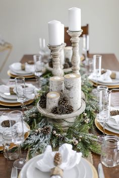 the table is set with candles, pine cones and white napkins on top of it