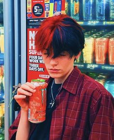 a young man with red hair holding a drink in front of a vending machine