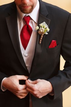 a man in a black suit with a red tie and boutonniere