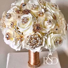 a bridal bouquet in white and gold with pearls on the bottom is sitting on a table