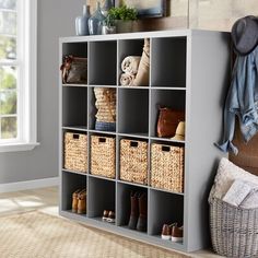 a shelf filled with baskets and shoes next to a wall mounted coat rack in a living room