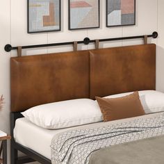 a bed with two framed pictures on the wall above it, and a brown leather headboard