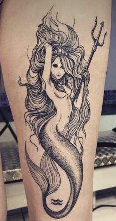 a woman with long hair and a mermaid tail tattoo on her leg, holding a spear