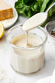 a spoon is pouring dressing into a small glass jar on a table with other ingredients