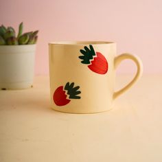 a coffee cup with strawberries painted on it next to a succulent plant