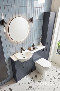 a white toilet sitting next to a bathroom sink under a round mirror on a wall