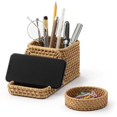 a basket with pens, pencils and glasses in it next to a cell phone