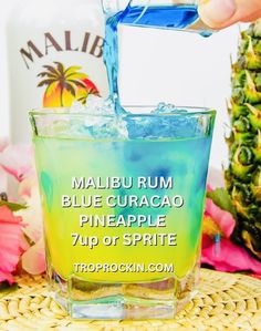 a person pouring blue curacao into a glass with pineapple syrup in it