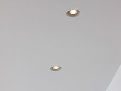 two lights that are on the ceiling in a room with white walls and flooring