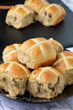 hot cross buns on a black plate with cinnamon sticks in the background and two plates full of them