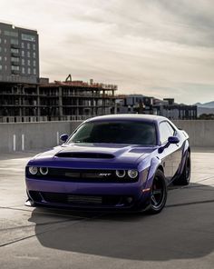 a purple car is parked in an empty parking lot with buildings in the back ground