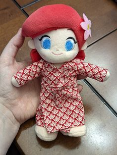 a hand holding a small red and white doll