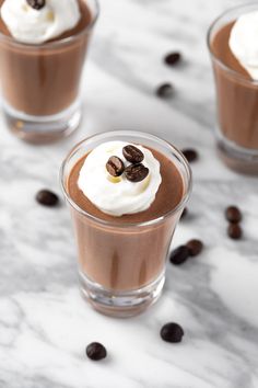 three glasses filled with chocolate pudding and whipped cream on top of coffee beans scattered around