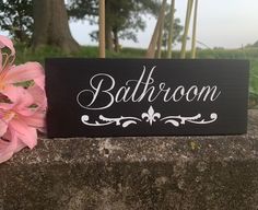 a bathroom sign sitting on top of a stone wall next to pink flowers and trees