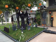 halloween decorations in front of a house with pumpkins hanging from the trees and on the lawn