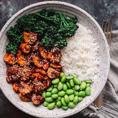 a white bowl filled with rice, broccoli and other vegetables next to a fork