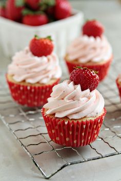 strawberry cupcakes with white frosting and strawberries on cooling rack next to bowl of strawberries