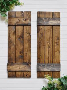 two wooden shutters on the side of a white building with flowers in front of them