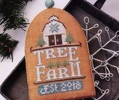 a cross stitch ornament sitting on top of a tray next to some pine branches