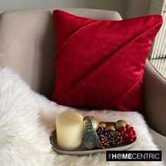 a tray with a candle, christmas decorations and pine cones sits on a chair next to a red pillow