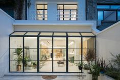 a large white house with lots of windows and plants in the front yard at night