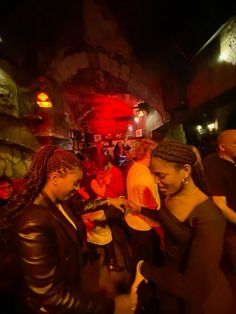 two women standing next to each other in front of a red light at a party